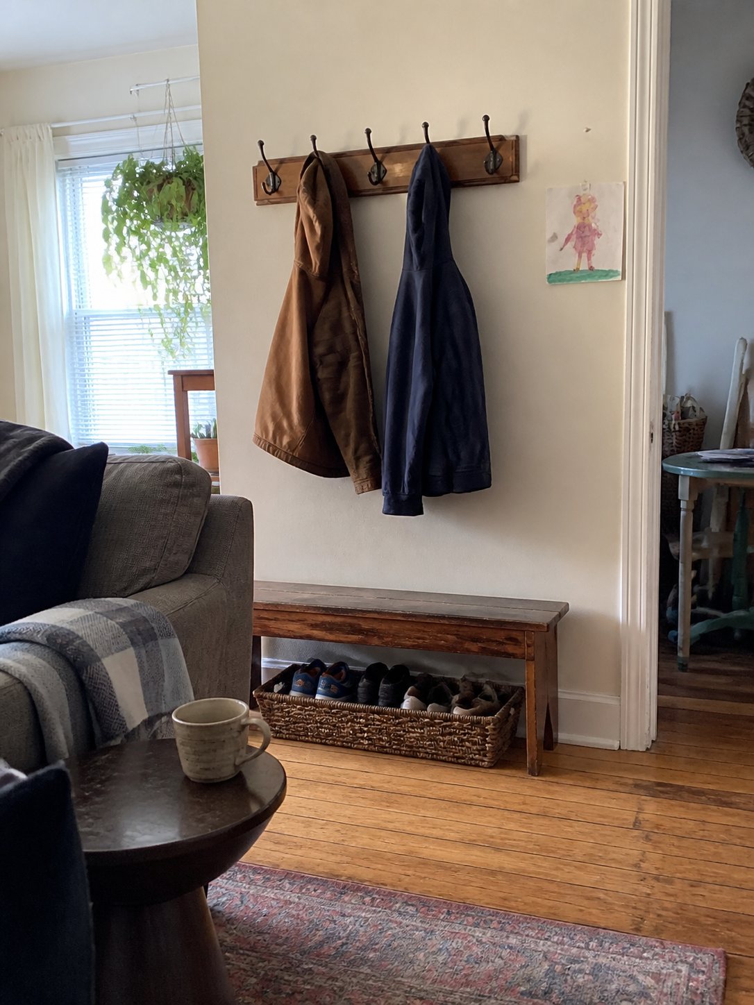 A lived-in home entryway with coat hooks, a bench, baskets, and soft afternoon light