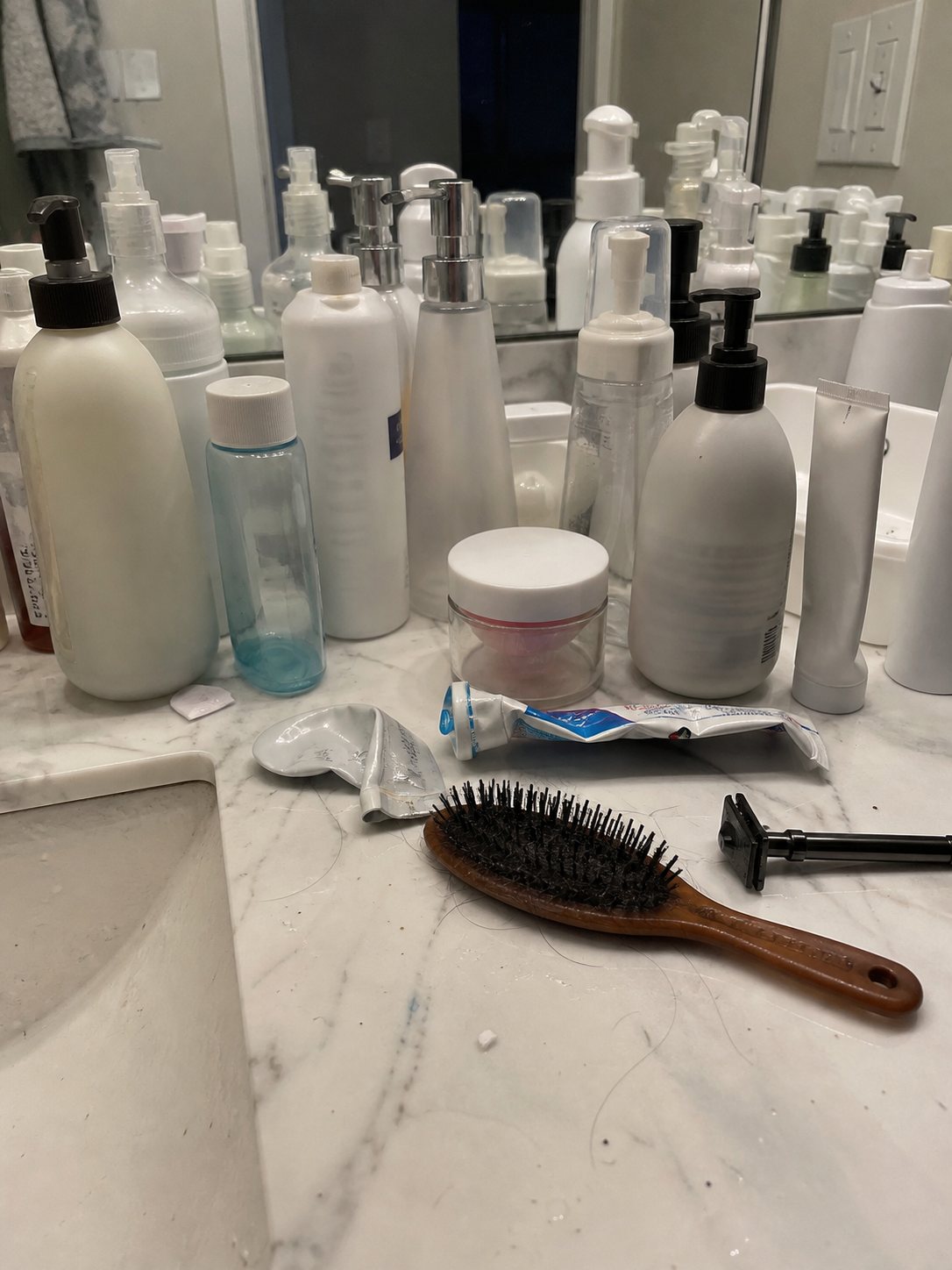 Crowded bathroom vanity with skincare bottles, makeup, and toiletries packed tightly together