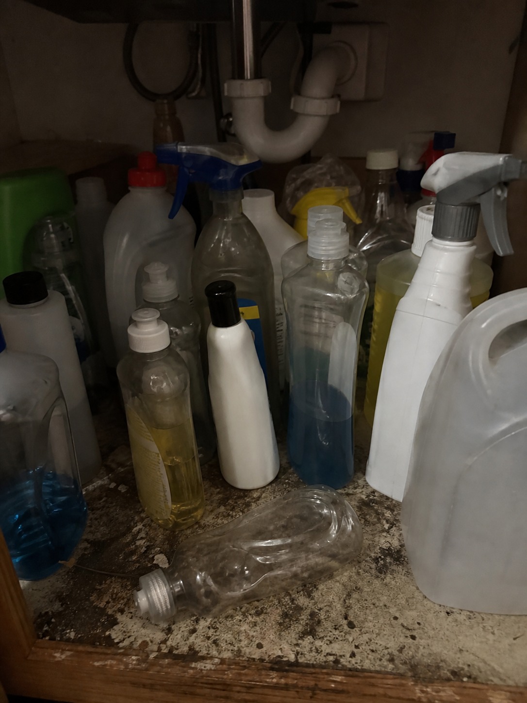 Cluster of empty plastic cleaning bottles under a kitchen sink cabinet