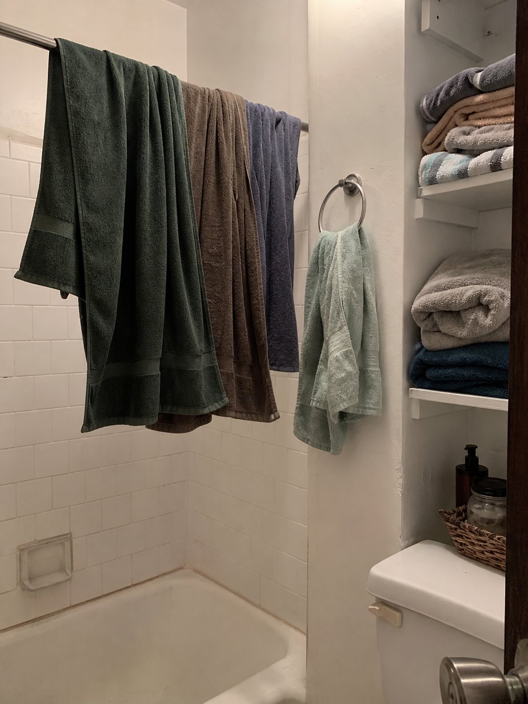 Bathroom with towels stacked on the floor and cluttered counter with no storage cabinet