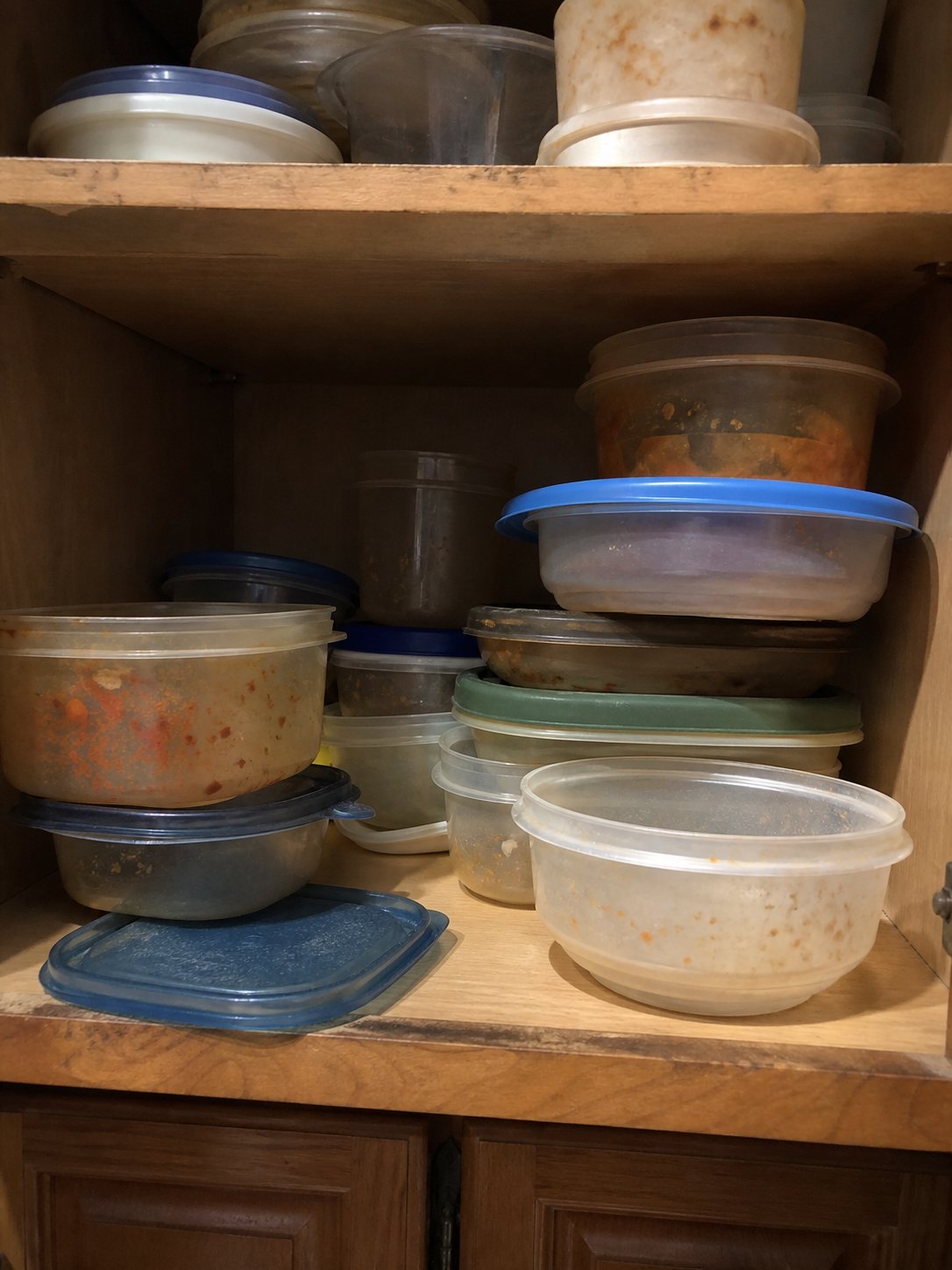 Mismatched plastic food containers and lids piled in a kitchen cabinet